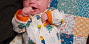 Roxas is registered to the contest to win money with this photo: baby, bed_cover, child, colorful, comfortable, cozy, cute, facial_expression, indoors, infant, lying_down, onesie, patchwork_quilt, patterned_fabric, portrait, sleepwear, small_hands, soft_lighting, space_theme, young