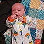 baby, bed_cover, child, colorful, comfortable, cozy, cute, facial_expression, indoors, infant, lying_down, onesie, patchwork_quilt, patterned_fabric, portrait, sleepwear, small_hands, soft_lighting, space_theme, young