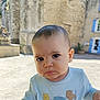 baby, child, face, outdoor, expression, pout, shirt, building, window, stone_wall, blue_shutters, person, portrait, daylight, cute, infant, casual_clothing, curious, young, head