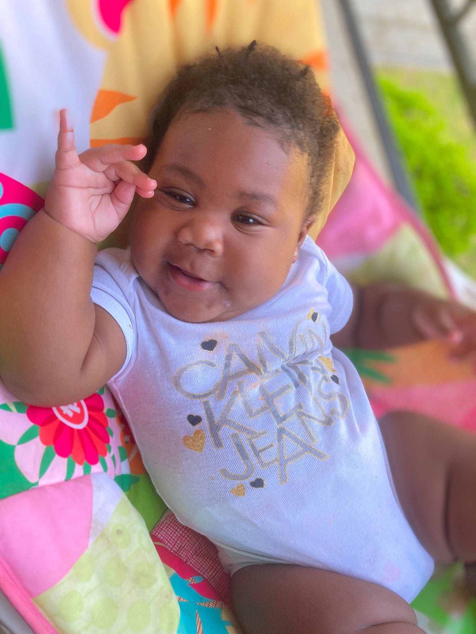Kennedi is registered to the contest to win money with this photo: baby, baby_toddler_clothing, bib, cheek, chin, dress, eye, facial_expression, finger, grass, hairstyle, hand, happy, lip, mouth, neck, person, pink, skin, smile