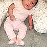 baby, infant, pink_clothing, socks, pillow, leaf_pattern, carpet, indoors, child, cute, portrait, soft_lighting, seated, young, person, small, curious, head_tilt, cozy, home