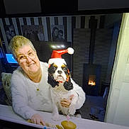 Vyvi participe au concours pour gagner de l'argent avec cette photo : candle, celebration, cozy, cupcake, dog, elderly_woman, family_photos, female, festive, fireplace, glasses, holiday, home_interior, indoor, pet, portrait, santa_hat, smiling, table, white_sweater