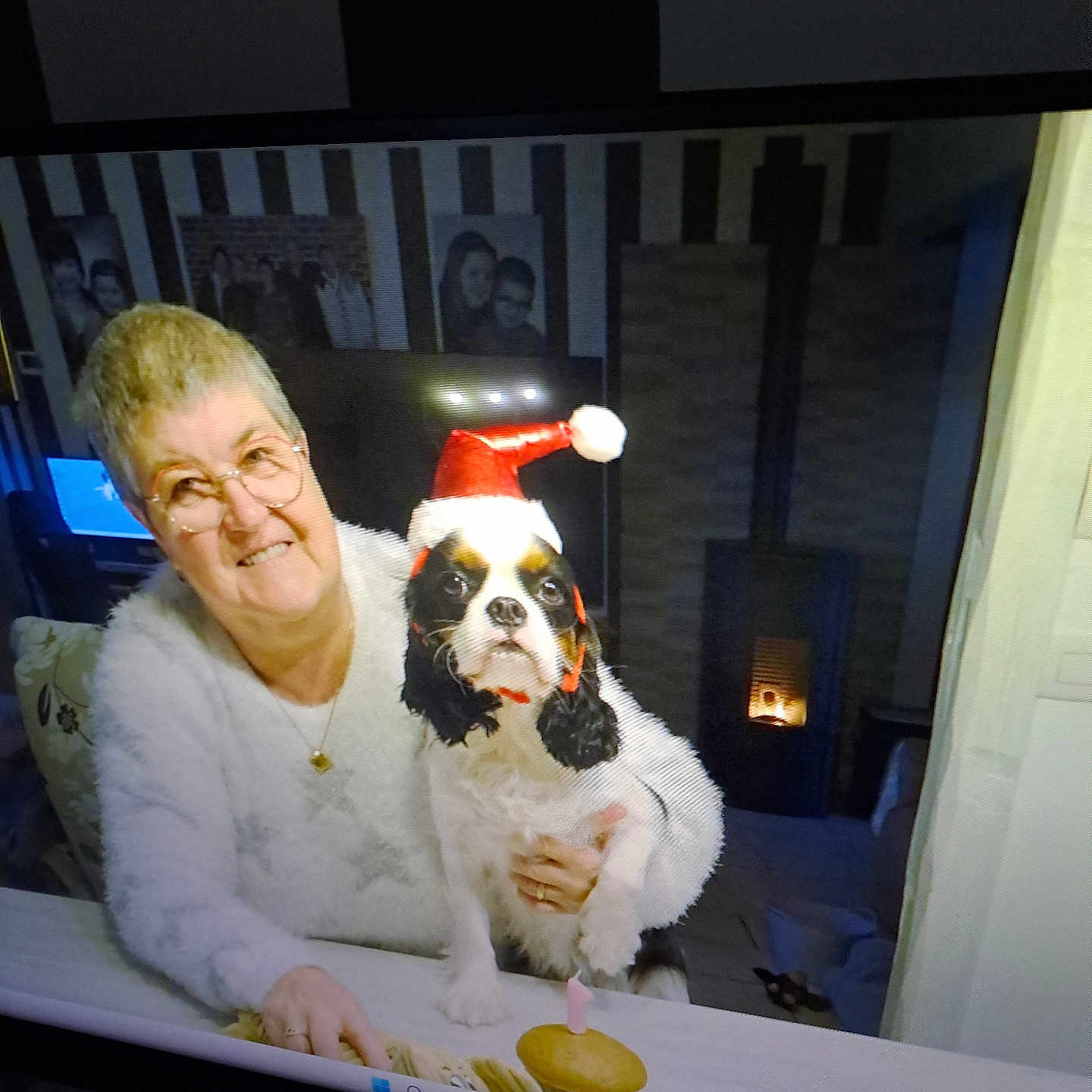 Vyvi participe au concours pour gagner de l'argent avec cette photo : candle, celebration, cozy, cupcake, dog, elderly_woman, family_photos, female, festive, fireplace, glasses, holiday, home_interior, indoor, pet, portrait, santa_hat, smiling, table, white_sweater