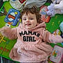 baby, child, pink_hoodie, smiling, play_mat, toy, stuffed_animal, colorful, happy, cute, indoor, face, person, infant, clothing, soft_toy, lying_down, expression, playtime, young_child