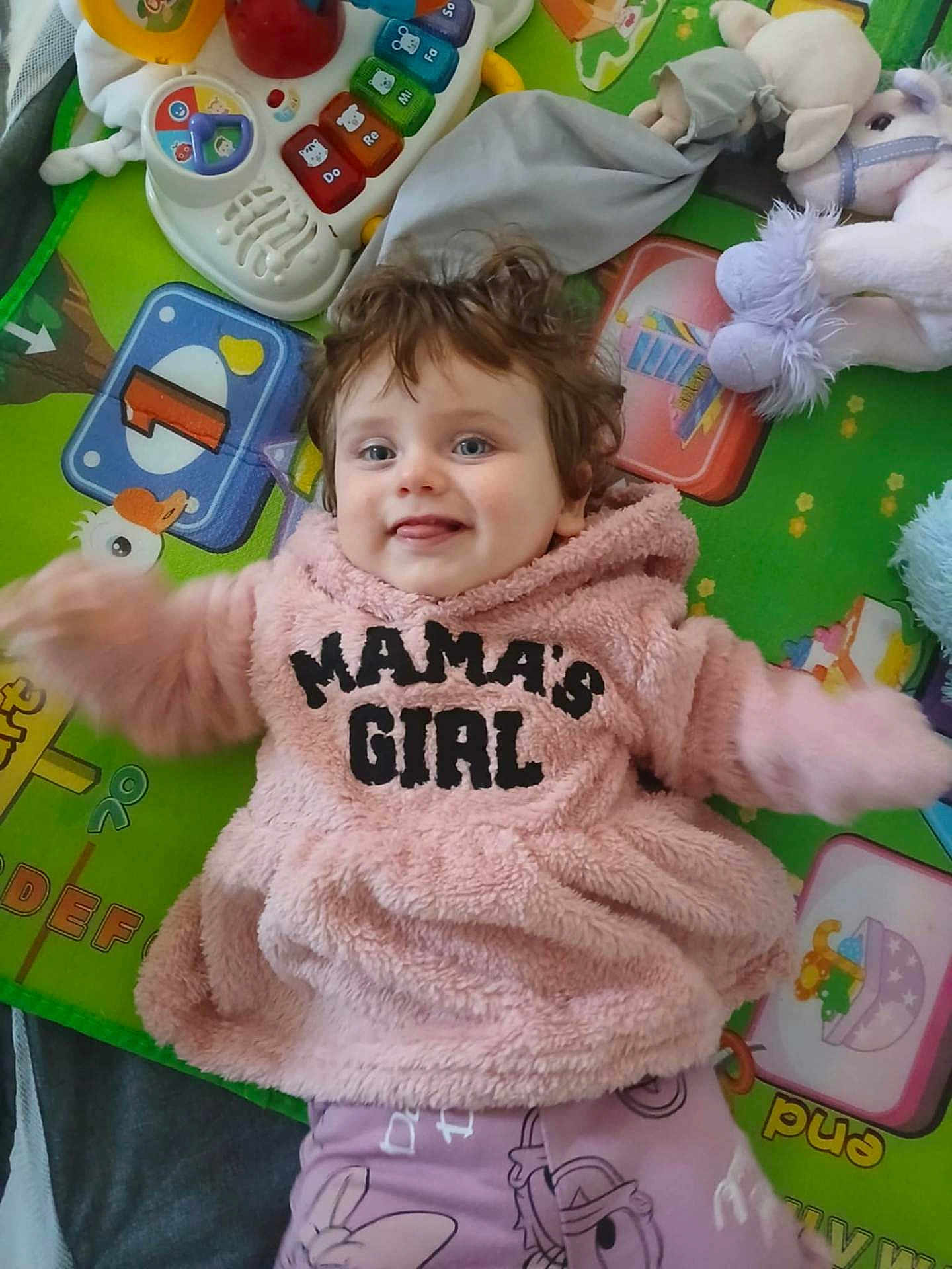 Scarlett-Raigh is registered to the contest to win money with this photo: baby, child, pink_hoodie, smiling, play_mat, toy, stuffed_animal, colorful, happy, cute, indoor, face, person, infant, clothing, soft_toy, lying_down, expression, playtime, young_child