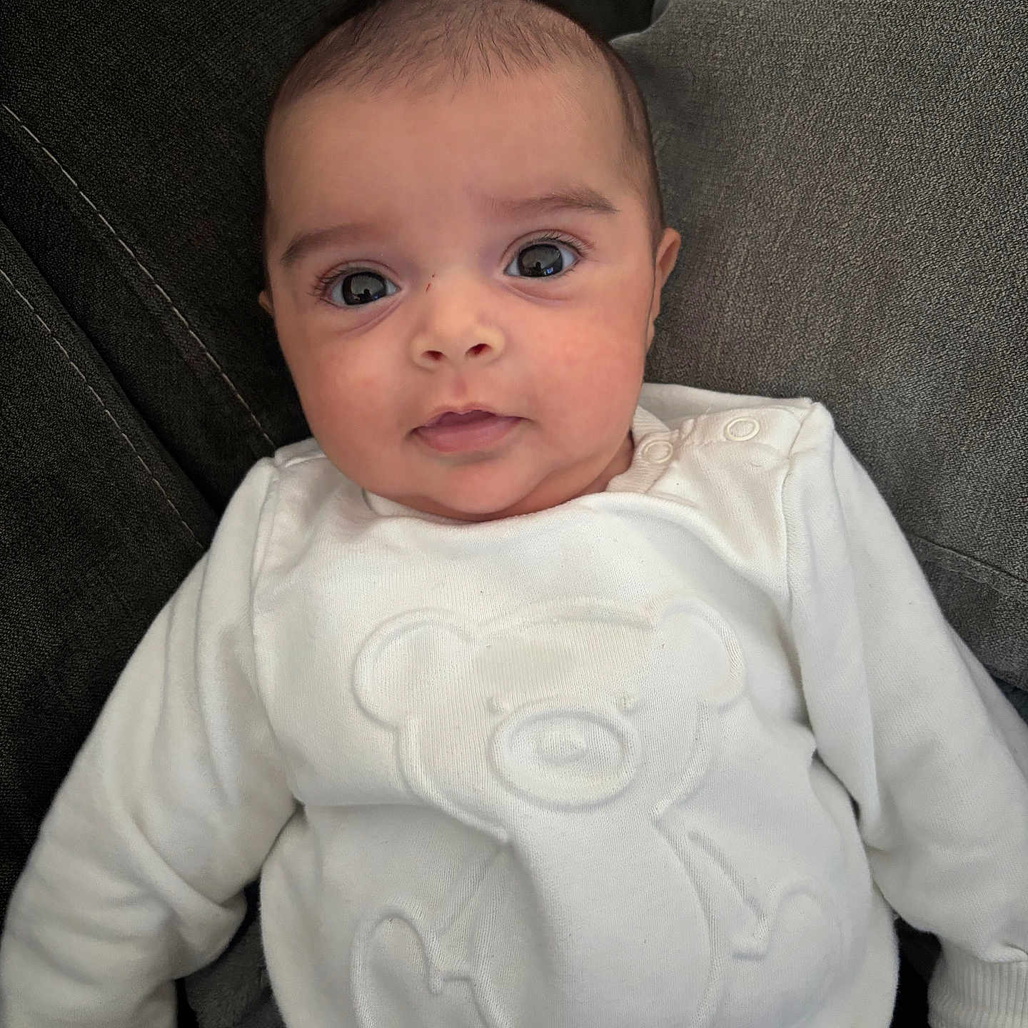 Aline participe au concours pour gagner de l'argent avec cette photo : baby, casual_clothing, child, comfortable, couch, cozy, cushion, cute, indoors, infant, person, portrait, relaxed, sitting, smile, soft_fabric, teddy_bear_design, white_sweater, wide_eyes, young_child