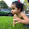Egypt is registered to the contest to win money with this photo: child, toddler, baby, crawling, grass, outdoor, portrait, face, curly_hair, red_bow, earring, serious_expression, playful, garden, lawn, green_car, suv, house, trees, daylight