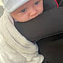 baby, infant, white_hat, blanket, blue_eyes, close_up, face, hand, car_seat, stroller, soft_texture, warm_clothing, candid, child, cute, outdoor, comfort, person, human, portrait
