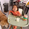 toddler, child, high_chair, messy, food, whipped_cream, smile, happy, golden_retriever, dog, kitchen, floor, drink_container, orange_clothing, table, chair, home, pet, indoor, baby