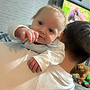 Reggie joined the competition — help win amazing prizes! baby, child, person, shoulder, white_shirt, indoor, living_room, television, toys, plush_toy, hand, face, hair, couch, brick_wall, smile, cute, infant, close_up, portrait
