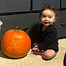 child, toddler, pumpkin, autumn, halloween, sitting, smiling, portrait, indoor, carpet, kitchen, cabinets, orange, black_clothing, curly_hair, barefoot, happy, seasonal, family_photo, still_life