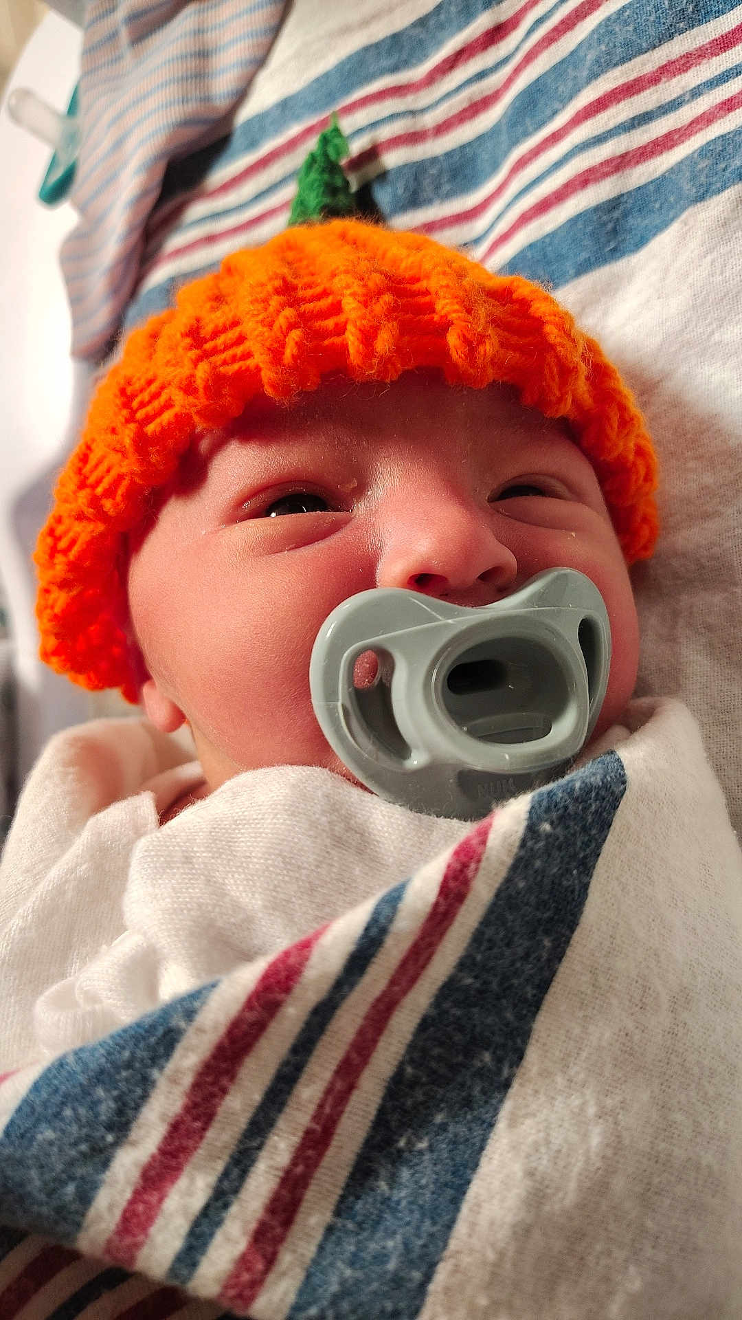 Noah joined the competition — help win amazing prizes! baby, newborn, pacifier, orange_hat, knitted_hat, blanket, striped_blanket, sleepy, close_up, face, infant, cute, cozy, soft, indoors, wrapped, headwear, child, person, portrait