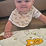 Noah is registered to the contest to win money with this photo: animal_prints, baby, bib, child, clothing, couch, curious, cute, face, floor, hand, head, indoor, infant, living_room, play_mat, smile, soft_toys, toddler, wooden_floor