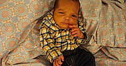 Kingston is registered to the contest to win money with this photo: baby, infant, child, portrait, lying_down, bed, bedding, blanket, patterned_fabric, plaid_shirt, black_pants, slippers, bear_slippers, hand, face, hair, indoors, bedroom, cute, resting