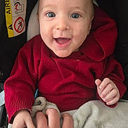 Charly participe au concours pour gagner de l'argent avec cette photo : baby, child, smile, happy, hand, red_sweater, blanket, car_seat, face, person, infant, clothing, cute, grip, interaction, warm, indoor, closeup, skin, expression