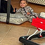 Julian is registered to the contest to win money with this photo: toddler, child, smiling, pajamas, dog, pet, cushion, floor, wood_floor, tile_floor, living_room, baby_walker, toy, furniture, home_interior, person, playful, cute, indoor, relaxed