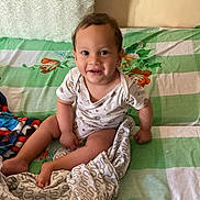 Kris Naidu Grandjean participe au concours pour gagner de l'argent avec cette photo : toddler, child, smiling, bed, blanket, book, toy, indoor, happy, person, face, clothing, fabric, pillow, floral_pattern, green, white, cozy, cute, portrait