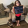Jax joined the competition — help win amazing prizes! barefoot, boy, casual_clothing, celebration, chalkboard, child, cushions, dog, first_grade, glasses, home, indoor, living_room, pet, red_shirt, shorts, sign, smiling, sofa, wooden_floor