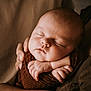 baby, sleeping, arms, hands, brown_cloth, newborn, peaceful, portrait, closeup, human, infant, skin, soft_light, resting, tender, emotion, care, comfort, warm, cuddle
