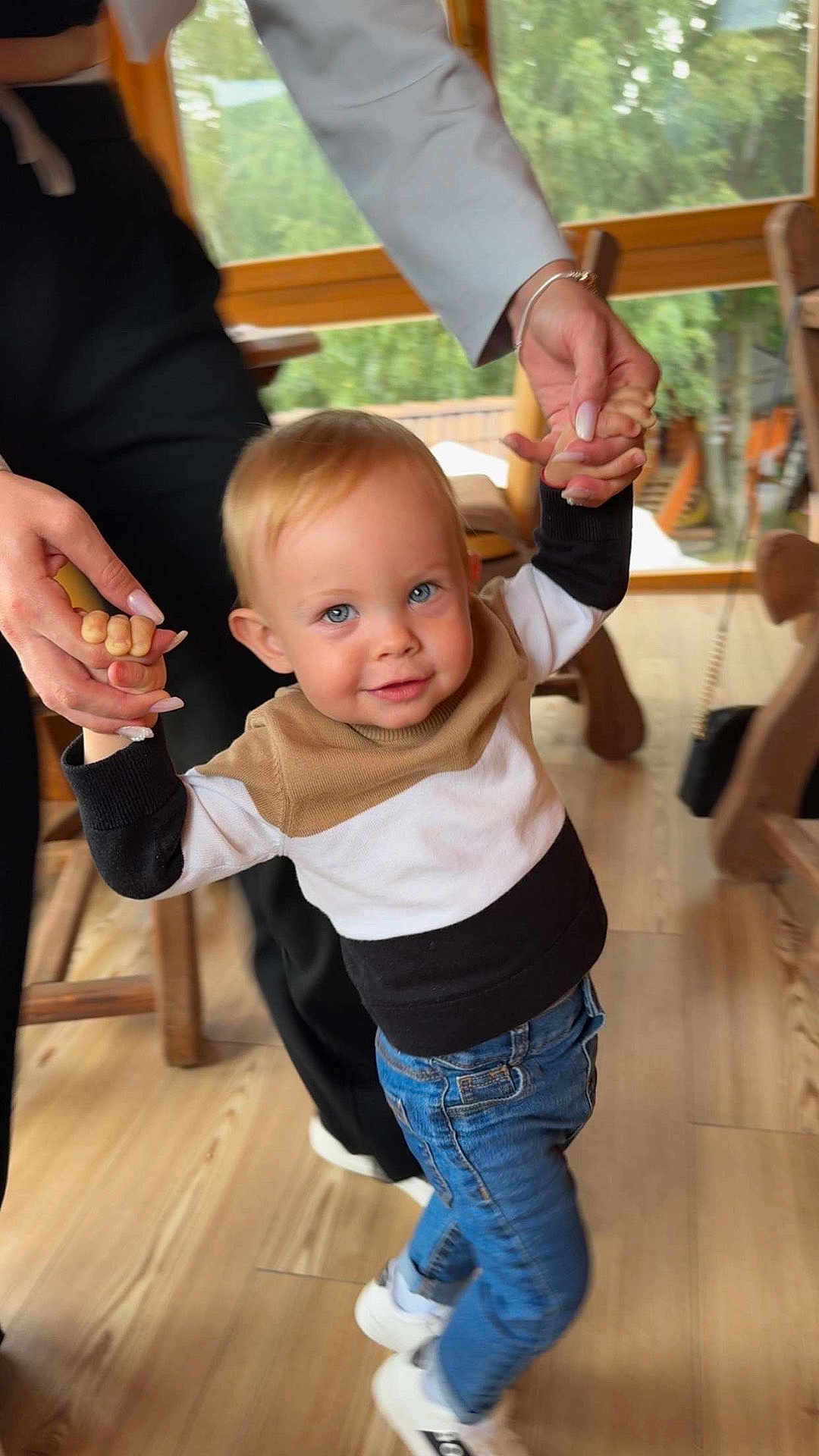 Elias a rejoint le concours — aidez-le/la à gagner de superbes lots ! child, toddler, blue_eyes, smiling, holding_hands, adult_hands, indoor, wooden_floor, jeans, sneakers, sweater, natural_light, window, furniture, casual_clothing, person, happy, playful, family, home