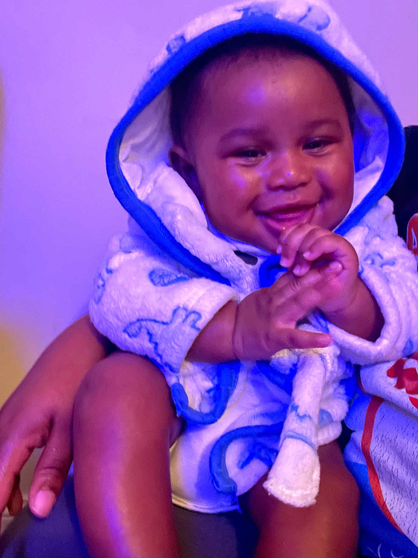 Johnte is registered to the contest to win money with this photo: baby, child, smiling, hooded_towel, clapping, hand, arm, leg, person, indoor, purple_light, happy, infant, cute, cozy, warm, sitting, skin, face, expression