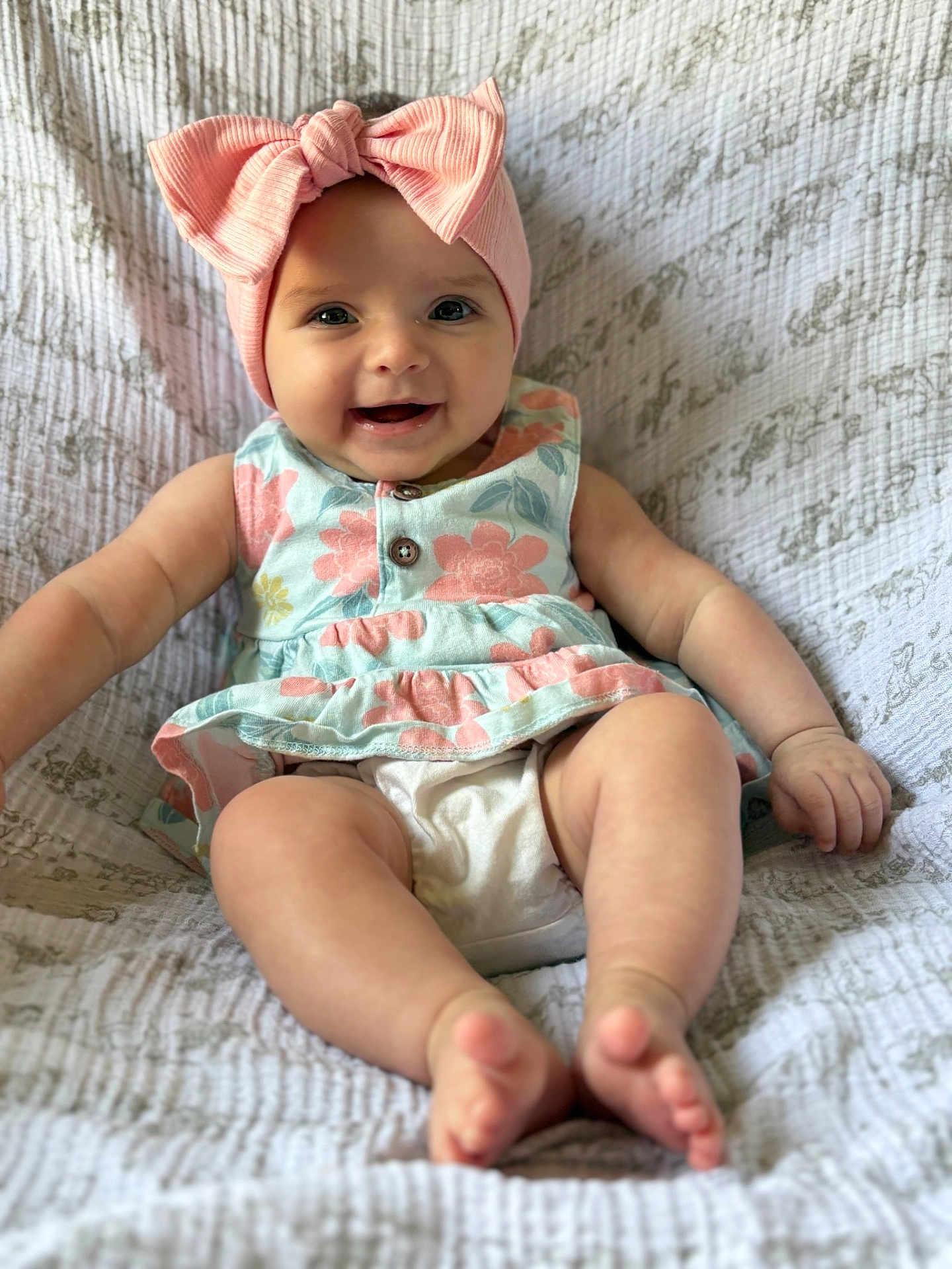 Anya is registered to the contest to win money with this photo: baby, child, smiling, headband, pink_bow, dress, floral_pattern, barefoot, sitting, blanket, cute, happy, portrait, infant, indoors, skin, person, legs, feet, closeup