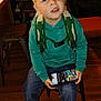 Kellen joined the competition — help win amazing prizes! child, boy, indoor, green_hoodie, backpack, smartphone, game, stool, wooden_floor, curious_expression, casual_clothing, jeans, black_shoes, white_laces, furniture, bookshelf, chair, table, room, person
