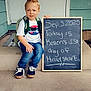 child, boy, backpack, chalkboard, porch, door, jeans, sneakers, tshirt, hair, spike_hairstyle, writing, announcement, step, outdoor, casual_clothing, smile, american_flag, heart_emoji, milestone