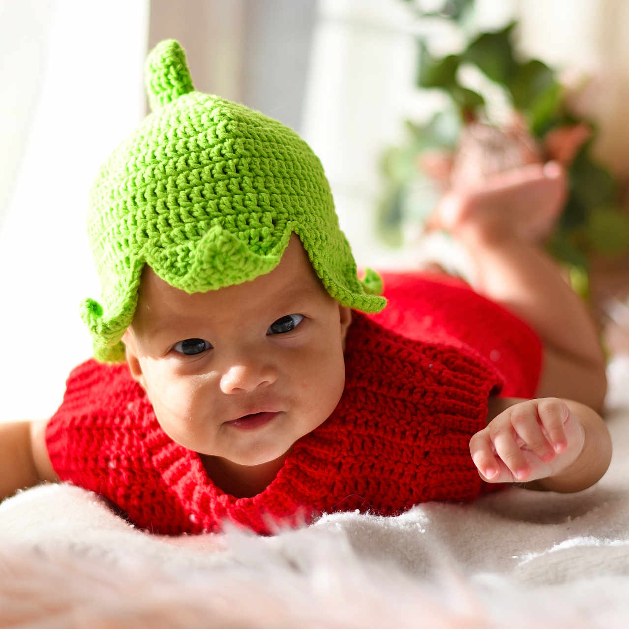 Asmara joined the competition — help win amazing prizes! baby, blanket, blurred_background, child, cozy, curious, cute, face, hand, headwear, home, indoor, infant, knitted_hat, lying_down, plants, portrait, red_sweater, skin, soft_texture
