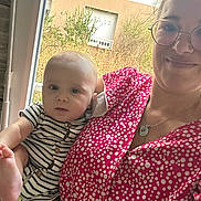 Sacha a rejoint le concours — aidez-le/la à gagner de superbes lots ! baby, building, casual, child, curious, face, glasses, holding, home, indoor, natural_light, necklace, person, plant, polka_dot_clothing, portrait, smile, striped_clothing, window, woman