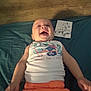 baby, laughing, tank_top, orange_pants, blanket, wooden_wall, sign, 5_mois, happy, infant, lying_down, child, clothing, smile, face, person, indoors, cute, playful, joyful
