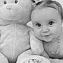baby, teddy_bear, plush_toy, child, cute, portrait, black_and_white, soft_texture, necklace, hand, face, smiling, toy, infant, cuddly, young_child, cute_expression, indoor, lying_down, hair_tie