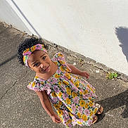 Aëlyah a rejoint le concours — aidez-le/la à gagner de superbes lots ! child, girl, dress, headband, floral_pattern, sidewalk, shadow, outdoor, sunlight, curly_hair, colorful, standing, concrete, wall, footwear, casual, expression, person, summer, daytime