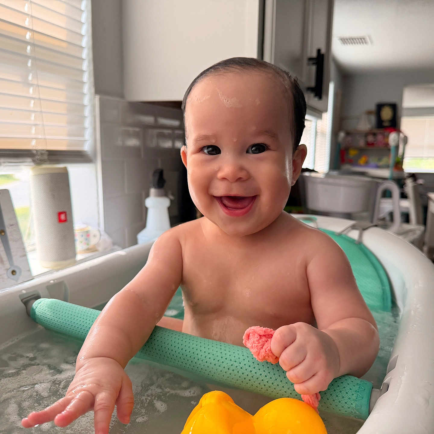 Lily Emelia joined the competition — help win amazing prizes! baby, bathtub, bath, child, smile, happy, water, toy, rubber_duck, kitchen, window, sunlight, sponge, indoor, person, infant, playful, cleaning, skin, arm