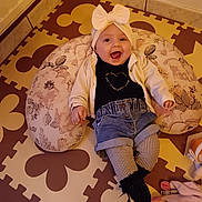 Esmée a rejoint le concours — aidez-le/la à gagner de superbes lots ! baby, black_socks, bow, cardigan, casual_clothing, child, cozy, cute, denim_shorts, floor_mat, floral_cushion, foam_puzzle_mat, happy, headband, indoor, infant, patterned_tights, person, playful, smiling