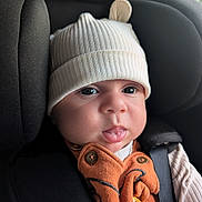 Daniel joined the competition — help win amazing prizes! baby, infant, hat, car_seat, black, orange_clothing, buttons, face, eyes, mouth, tongue, ribbed_hat, cute, child, seat_belt, closeup, indoors, young_child, person, apparel