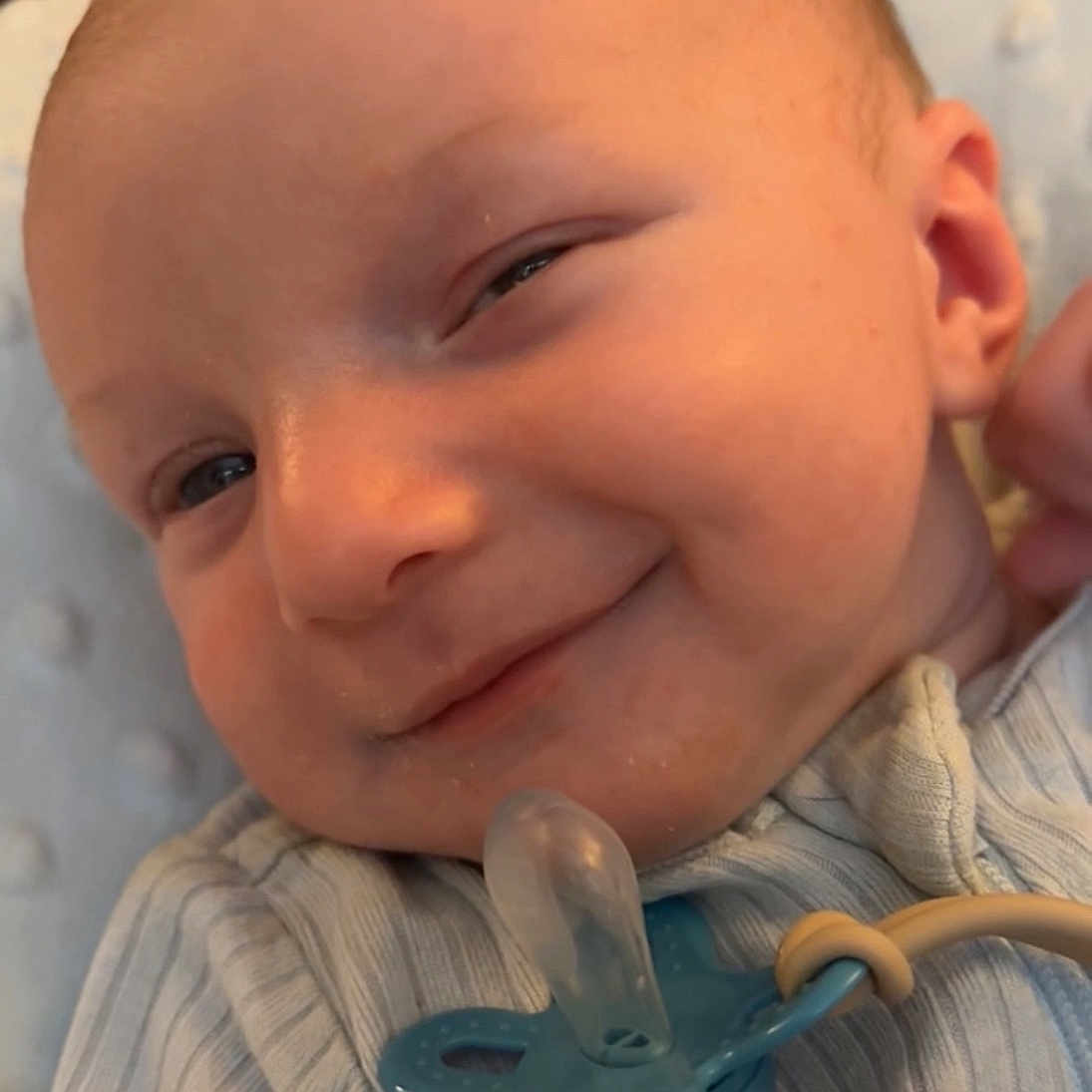 Rook is registered to the contest to win money with this photo: baby, blanket, cheeky, closeup, clothing, cute, expression, face, hand, head, indoors, infant, lying, newborn, onesie, pacifier, portrait, skin, smile, striped