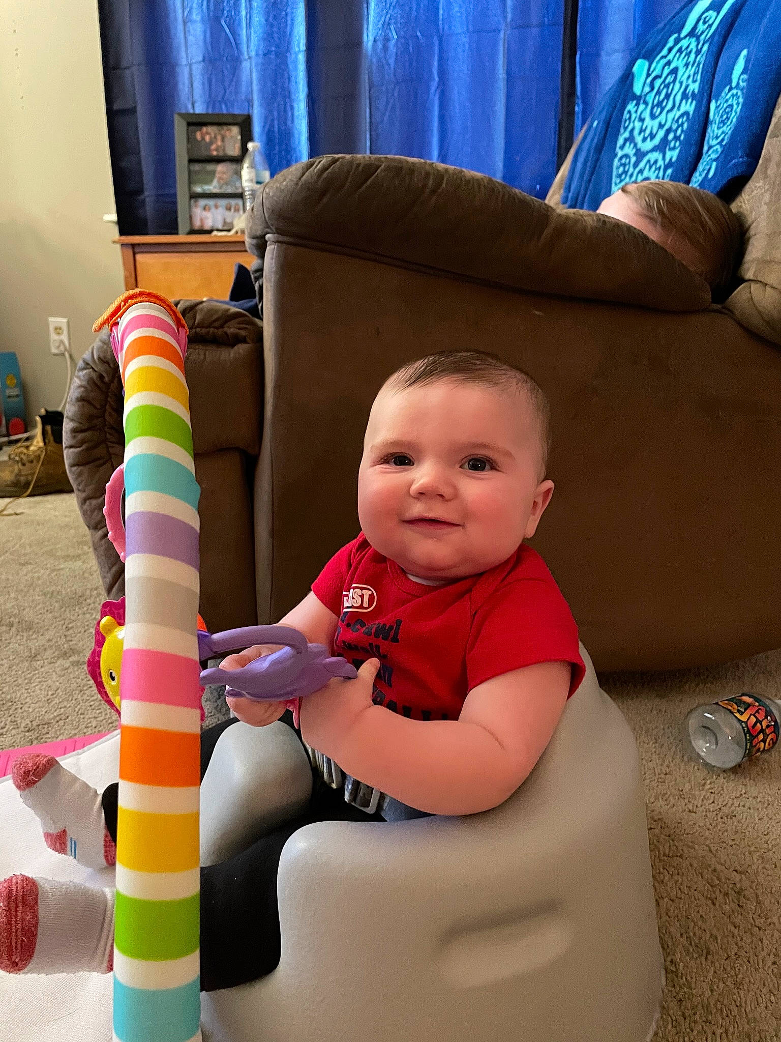Dakotah is registered to the contest to win money with this photo: baby, baby_playing_with_toys, baby_products, baby_toddler_clothing, blue, child, comfort, couch, curtain, flooring, fun, joy, lamp, lap, person, room, sitting, smile, television, thigh