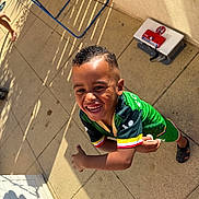 Nidhoimi Farrel a rejoint le concours — aidez-le/la à gagner de superbes lots ! child, smiling, green_clothing, short_hair, outdoor, sunlight, shadow, tile_floor, barefoot, sportswear, happy, boy, playful, patio, casual, daylight, person, expression, motion, background