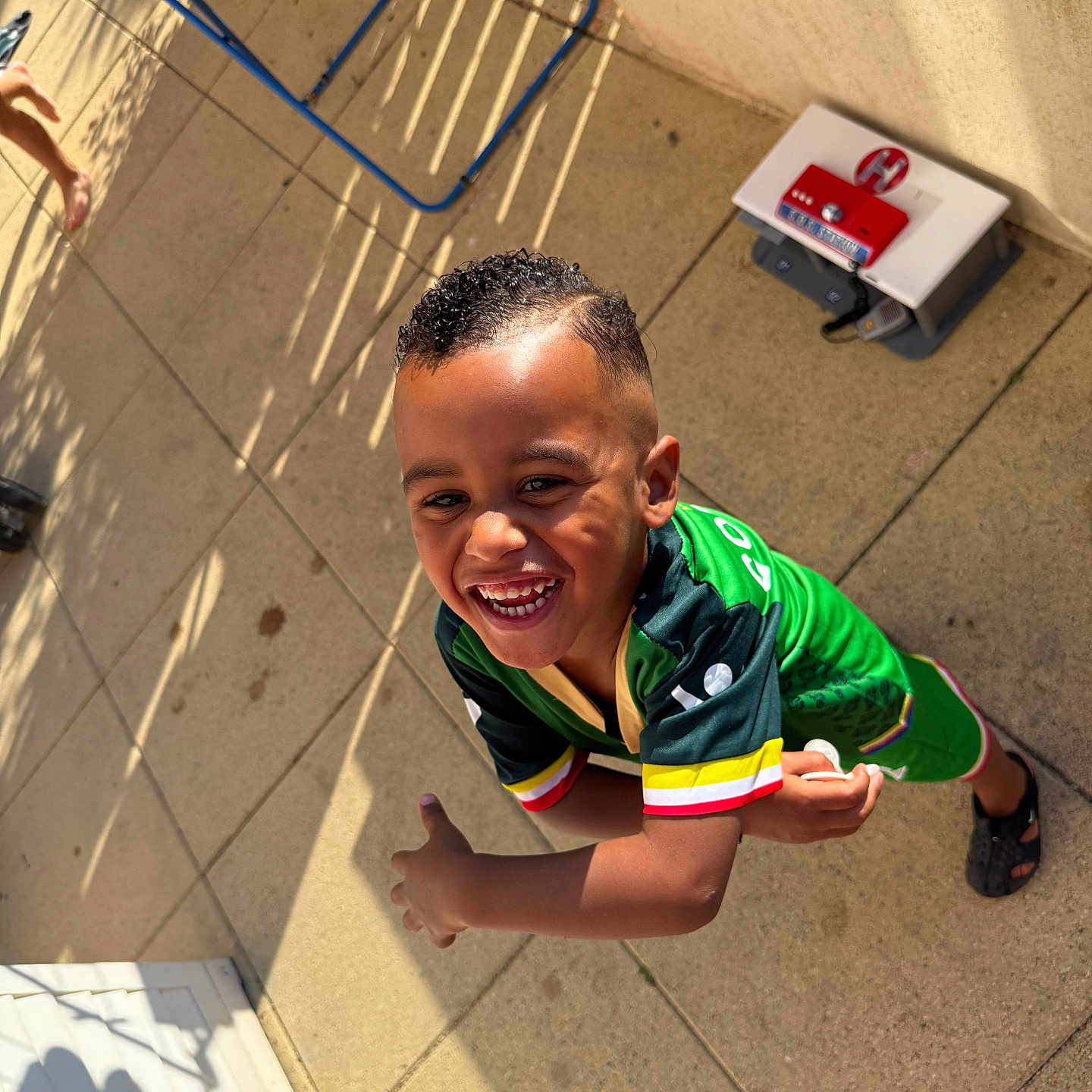 Nidhoimi Farrel a rejoint le concours — aidez-le/la à gagner de superbes lots ! background, barefoot, boy, casual, child, daylight, expression, green_clothing, happy, motion, outdoor, patio, person, playful, shadow, short_hair, smiling, sportswear, sunlight, tile_floor