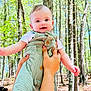 baby, child, person, forest, trees, nature, outdoor, green_overalls, smile, happy, hands, woman, background, sunlight, daylight, woodland, cute, holding, apparel, portrait