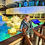 Aida is registered to the contest to win money with this photo: baby, child, denim_jacket, aquarium, rocks, water, concrete, adult_hands, blue_lighting, fish_tank, exhibit, indoor, person, holding, curious, casual_clothing, short_hair, watch, railing, museum