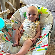 Colton joined the competition — help win amazing prizes! baby, infant, smiling, onesie, baby_seat, plush_toy, living_room, carpet, couch, curtain, floor, head, face, foot, hand, person, indoor, colorful, patterned, comfort