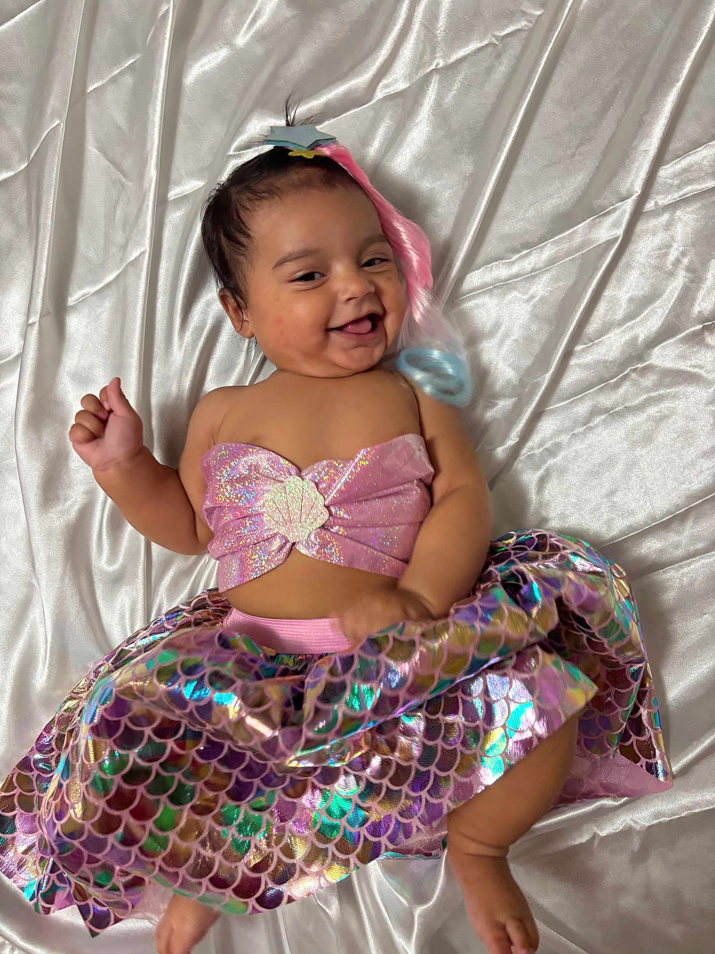 Alysha joined the competition — help win amazing prizes! baby, smiling, mermaid_costume, pink_top, iridescent_skirt, lying_down, silky_sheet, happy, cute, infant, colorful, playful, portrait, child, costume, hair_accessory, glitter, fabric, skin, one_person