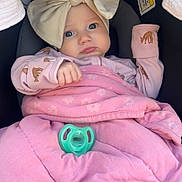 Logan is registered to the contest to win money with this photo: baby, infant, child, car_seat, blanket, bow, headband, pacifier, pink, clothing, cute, face, portrait, sleepsuit, safety_warning, indoor, person, young_child, expression, wrapped