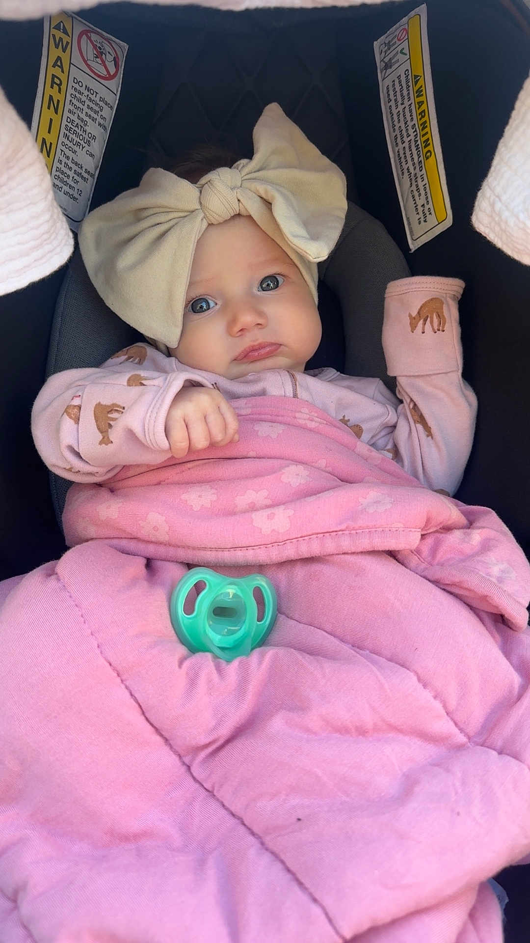 Logan is registered to the contest to win money with this photo: baby, infant, child, car_seat, blanket, bow, headband, pacifier, pink, clothing, cute, face, portrait, sleepsuit, safety_warning, indoor, person, young_child, expression, wrapped