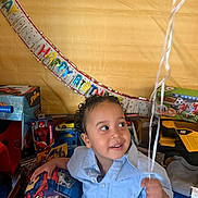 Khi is registered to the contest to win money with this photo: toddler, child, birthday, balloon, toy, curly_hair, blue_shirt, indoor, party, smiling, decorations, present, spiderman, truck, soccer, happy, face, hand, celebration, gift