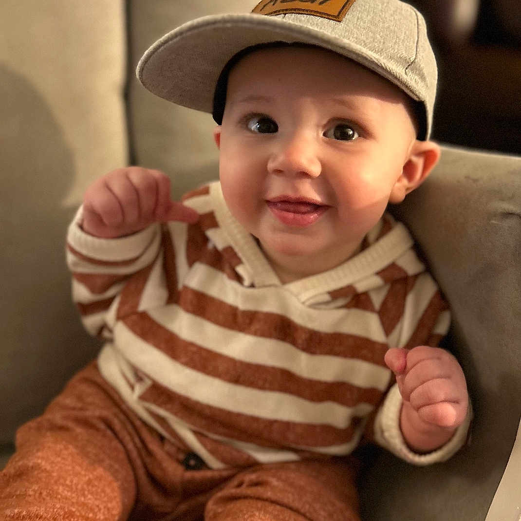 Azai is registered to the contest to win money with this photo: baby, baseballcap, bodypart, cap, clothing, couch, cushion, face, finger, furniture, hand, happy, hat, head, homedecor, pants, person, photography, portrait, sitting