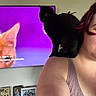 Sussie is registered to the contest to win money with this photo: woman, black_cat, cat, television, text_overlay, smile, indoor, portrait, shoulder, purple_hair, tank_top, framed_photos, living_room, pet, animal, face, head, feline, domestic_cat, casual