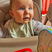 Elio a rejoint le concours — aidez-le/la à gagner de superbes lots ! baby, high_chair, bib, blue_eyes, indoor, toy, curious, child, infant, seated, clothing, face, expression, person, furniture, red_curtain, soft_light, closeup, cute, young_child